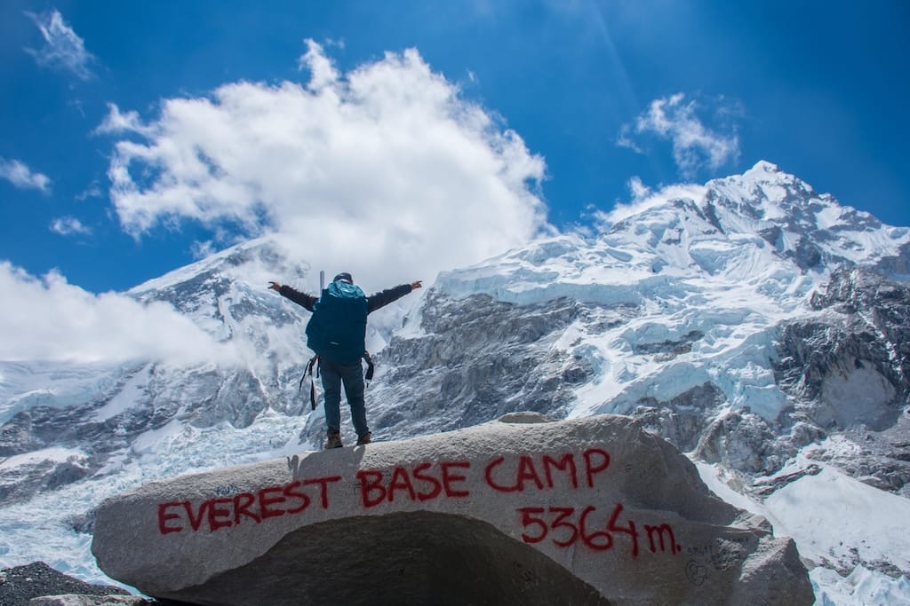 Trekker at Everest Base Camp beside large stone