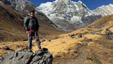 Solo trekker in silhouette reflecting at sunrise over Annapurna peaks, a moment of enlightenment captured in detail.